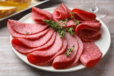 Photo of Slices of delicious sausage with thyme served on light wooden table, closeup