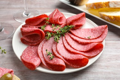 Photo of Slices of delicious sausage with thyme served on light wooden table, closeup
