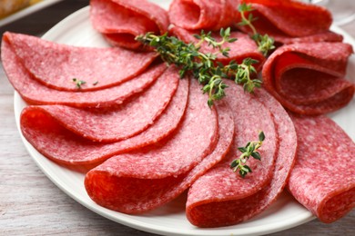 Photo of Slices of delicious sausage with thyme served on light wooden table, closeup