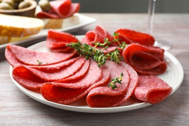 Photo of Slices of delicious sausage with thyme served on light wooden table, closeup