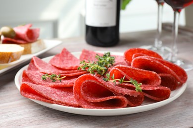 Photo of Slices of delicious sausage with thyme served on light wooden table, closeup