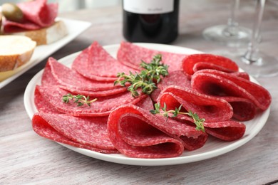 Photo of Slices of delicious sausage with thyme served on light wooden table, closeup