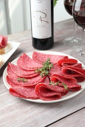 Photo of Slices of delicious sausage with thyme served on light wooden table