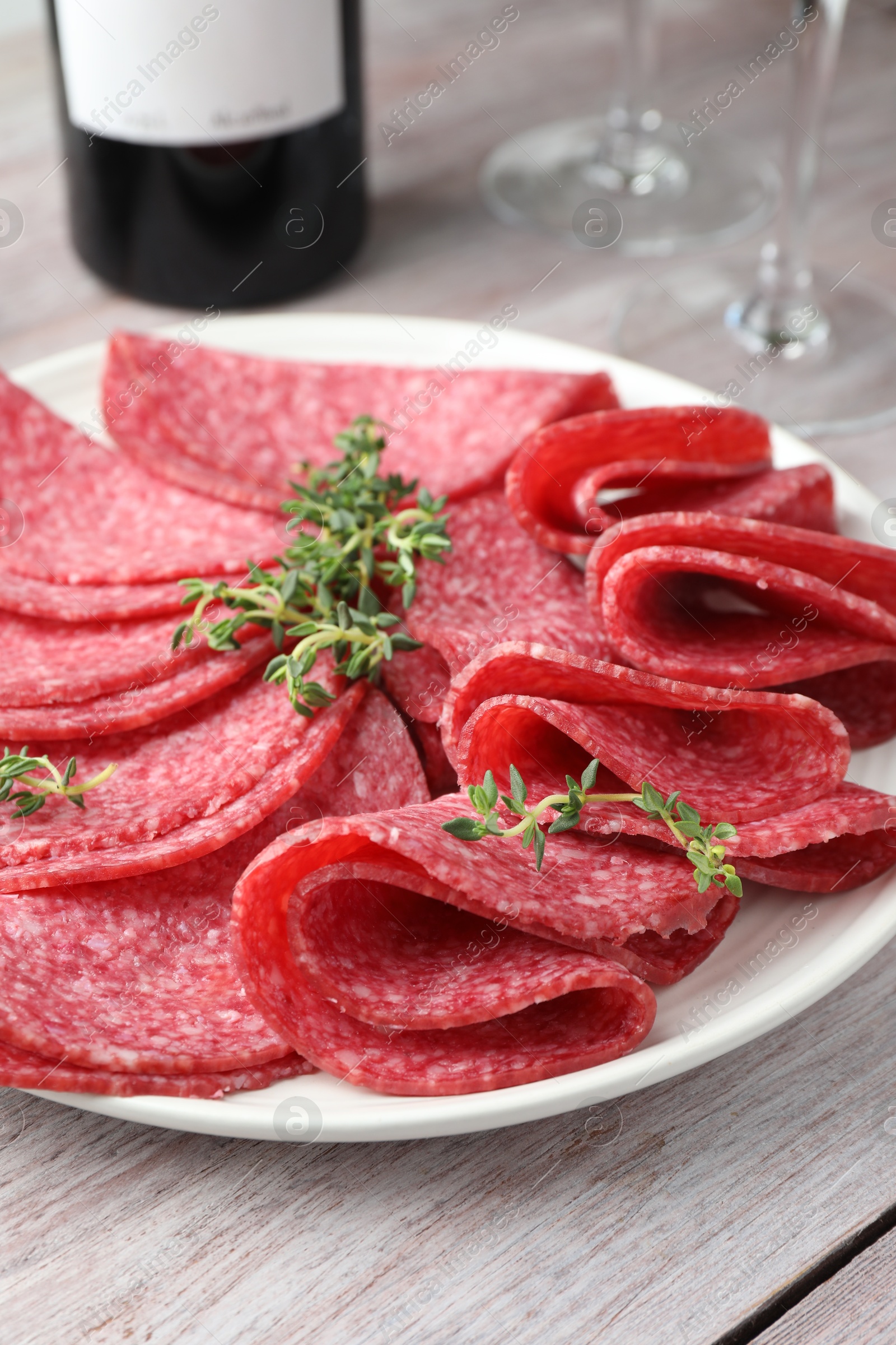 Photo of Slices of delicious sausage with thyme served on light wooden table, closeup