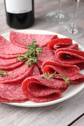 Photo of Slices of delicious sausage with thyme served on light wooden table, closeup