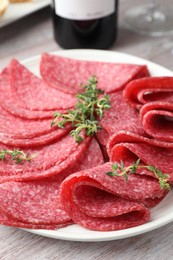 Photo of Slices of delicious sausage with thyme served on light wooden table, closeup