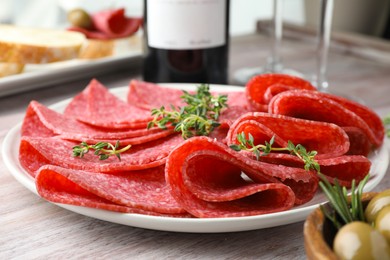 Photo of Slices of delicious sausage with thyme served on light wooden table, closeup