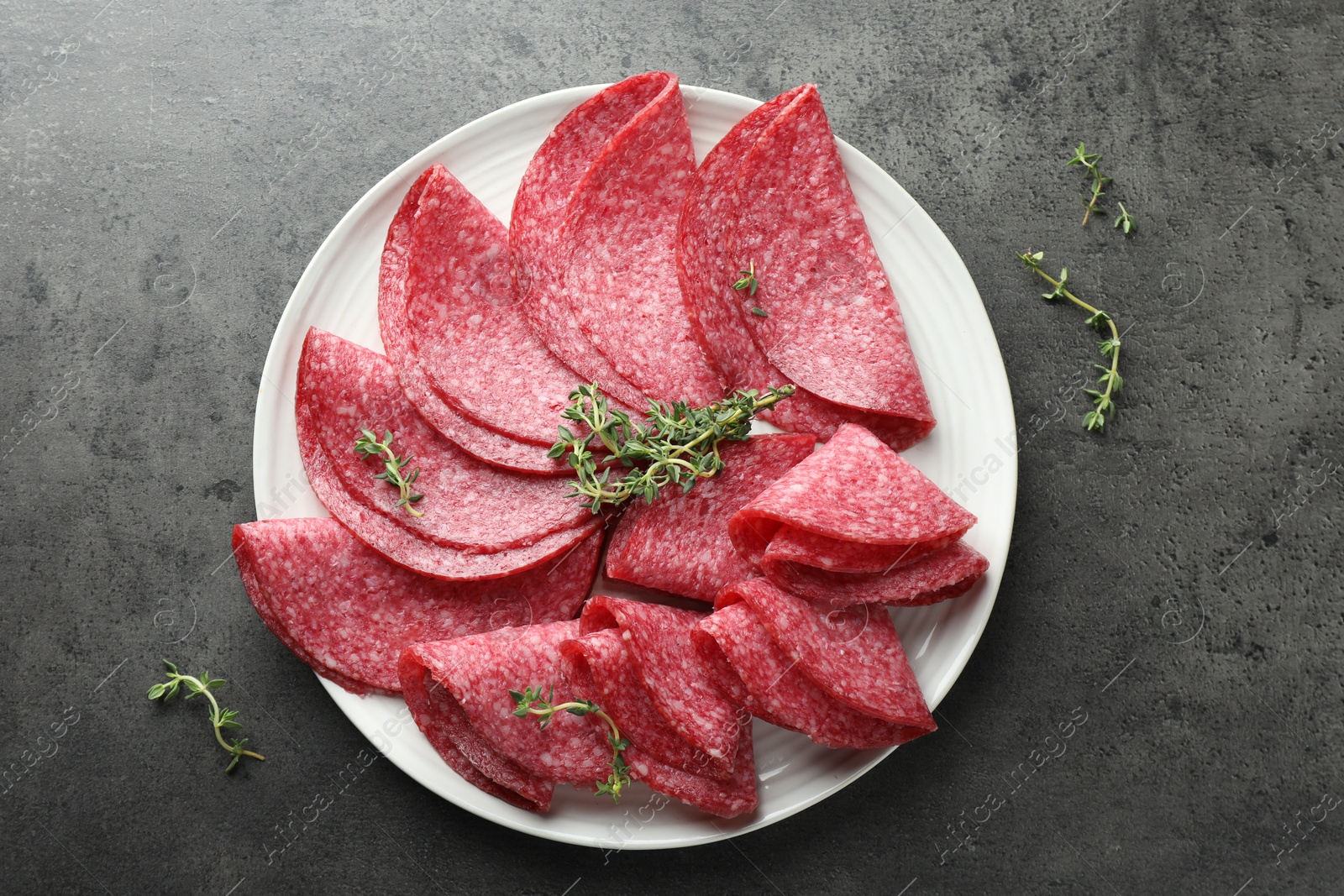 Slices of delicious sausage with thyme served on grey table, top view Photo of Slices of delicious sausage with thyme served on grey table, top view