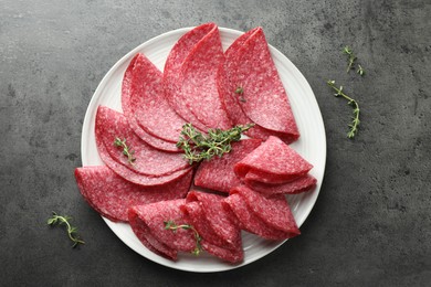Photo of Slices of delicious sausage with thyme served on grey table, top view