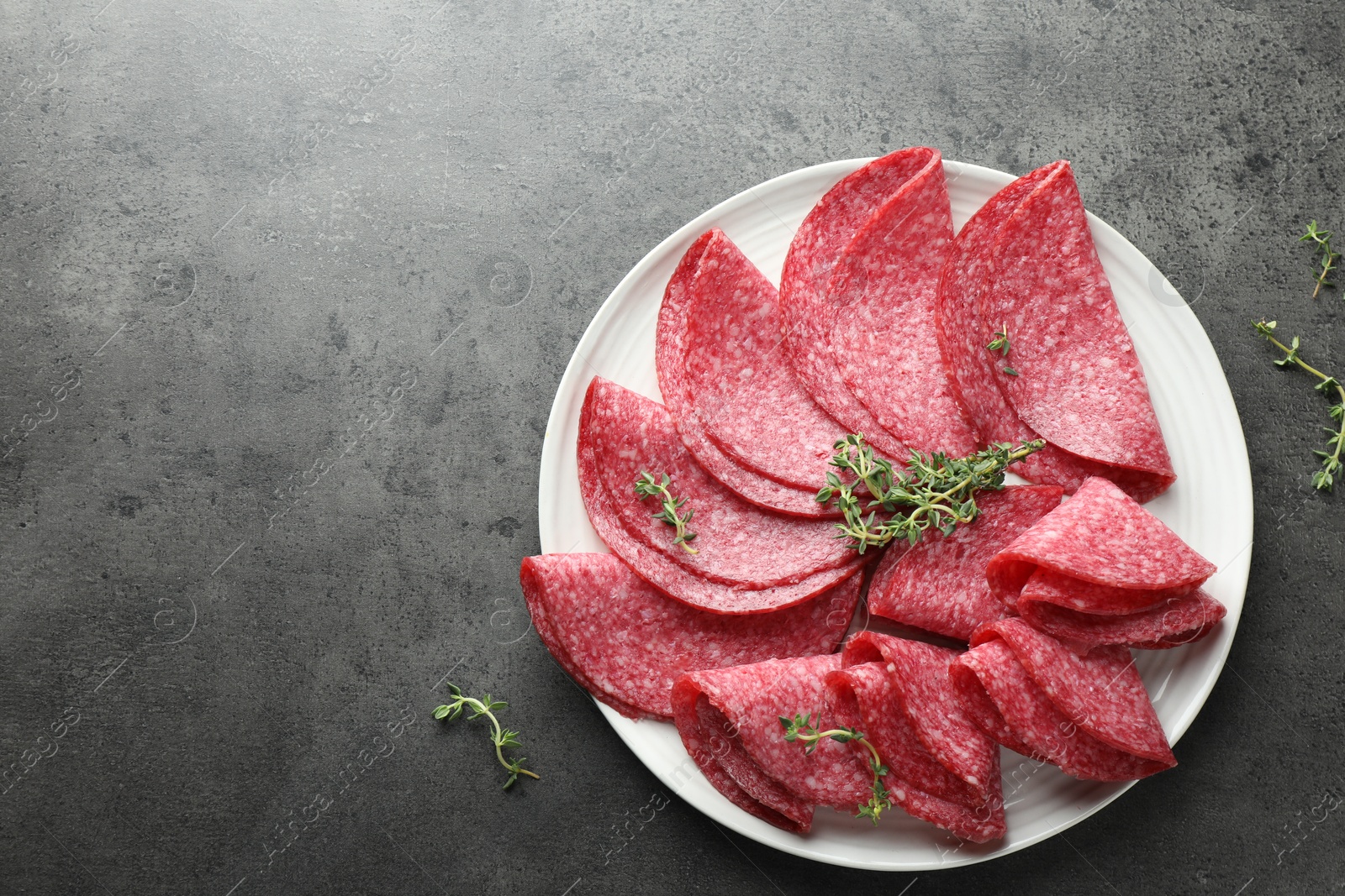 Photo of Slices of delicious sausage with thyme served on grey table, top view. Space for text