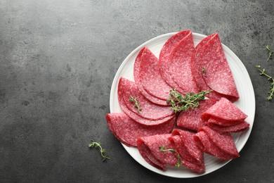 Photo of Slices of delicious sausage with thyme served on grey table, top view. Space for text