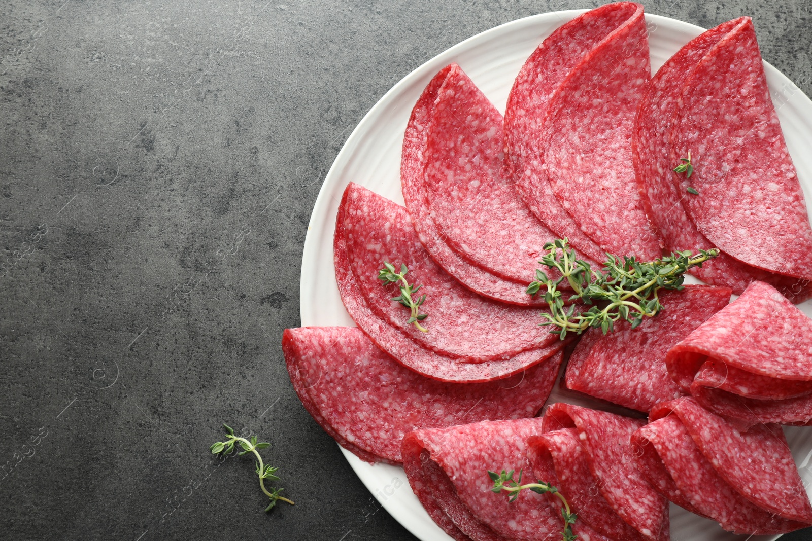 Photo of Slices of delicious sausage with thyme served on grey table, top view. Space for text