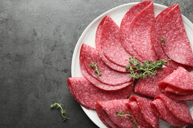 Photo of Slices of delicious sausage with thyme served on grey table, top view. Space for text