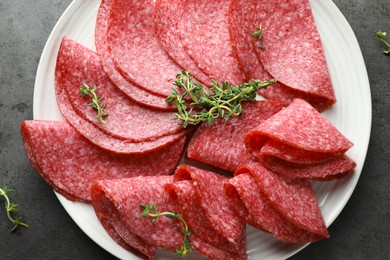 Photo of Slices of delicious sausage with thyme served on grey table, top view