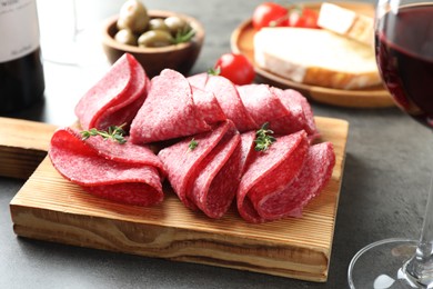Photo of Slices of delicious sausage with thyme served on grey table, closeup