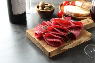 Photo of Slices of delicious sausage with thyme served on grey table