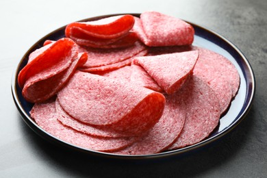 Photo of Slices of delicious sausage served on grey table, closeup