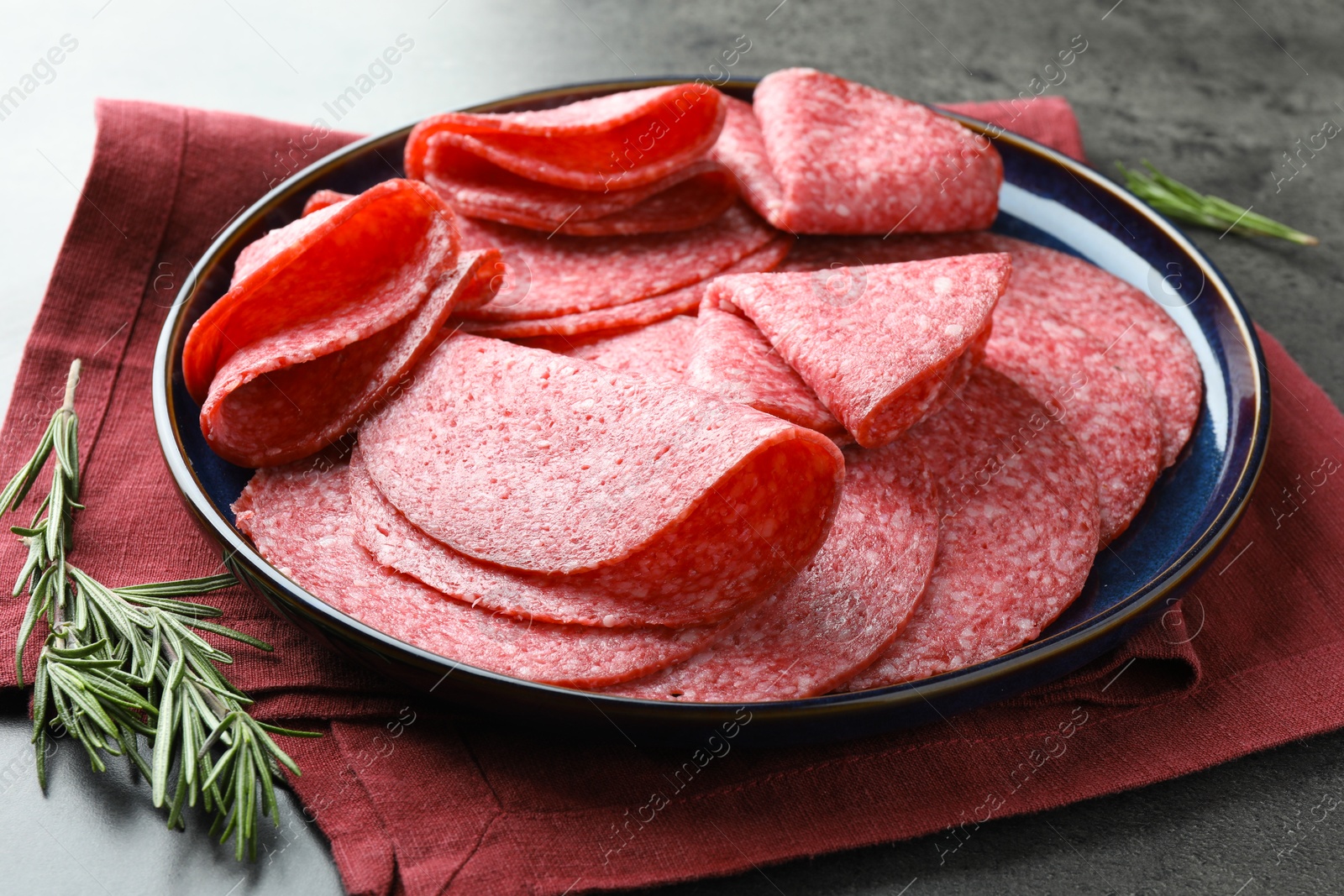 Photo of Slices of delicious sausage served on grey table, closeup