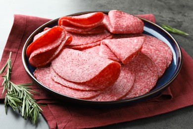 Photo of Slices of delicious sausage served on grey table, closeup