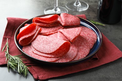 Photo of Slices of delicious sausage served on grey table, closeup