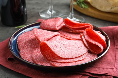 Photo of Slices of delicious sausage served on grey table, closeup