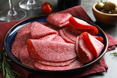 Photo of Slices of delicious sausage served on grey table, closeup