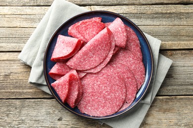Photo of Slices of delicious sausage on wooden table, top view