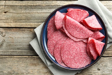 Photo of Slices of delicious sausage on wooden table, top view