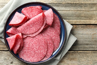 Photo of Slices of delicious sausage on wooden table, top view