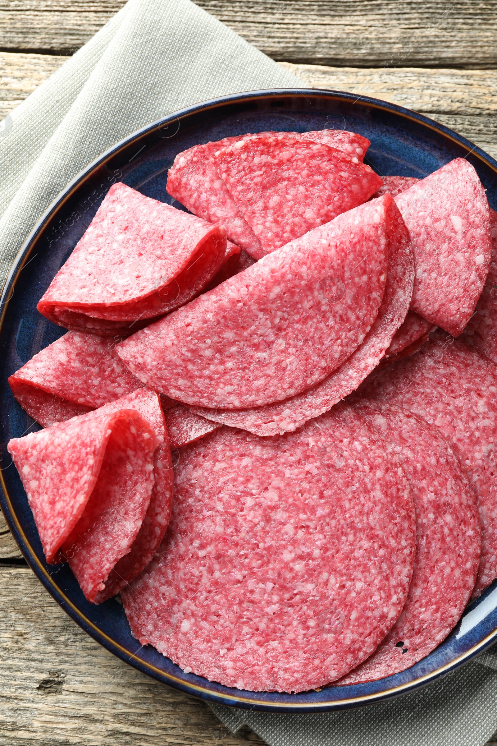 Photo of Slices of delicious sausage on wooden table, top view