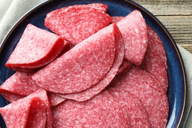 Photo of Slices of delicious sausage on wooden table, top view