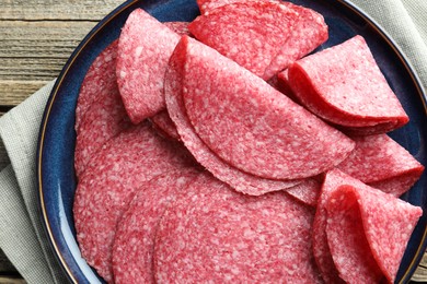 Photo of Slices of delicious sausage on wooden table, top view