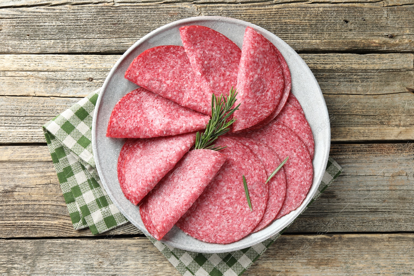 Photo of Slices of delicious sausage with rosemary served on wooden table, top view