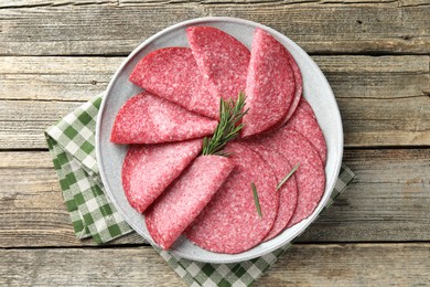 Photo of Slices of delicious sausage with rosemary served on wooden table, top view
