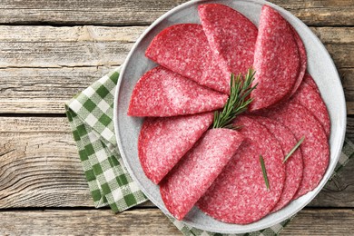 Photo of Slices of delicious sausage with rosemary served on wooden table, top view