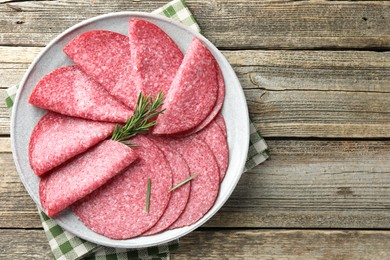 Photo of Slices of delicious sausage with rosemary served on wooden table, top view