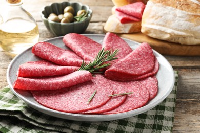Photo of Slices of delicious sausage with rosemary served on wooden table, closeup