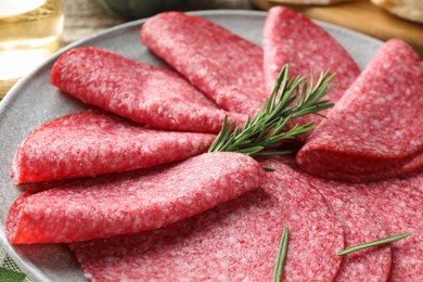 Photo of Slices of delicious sausage with rosemary served on table, closeup