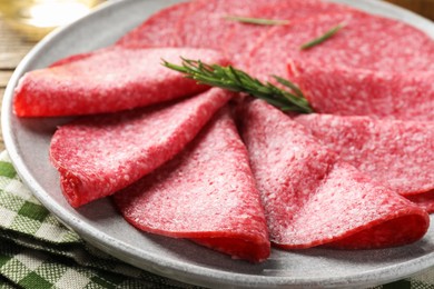 Photo of Slices of delicious sausage with rosemary served on table, closeup