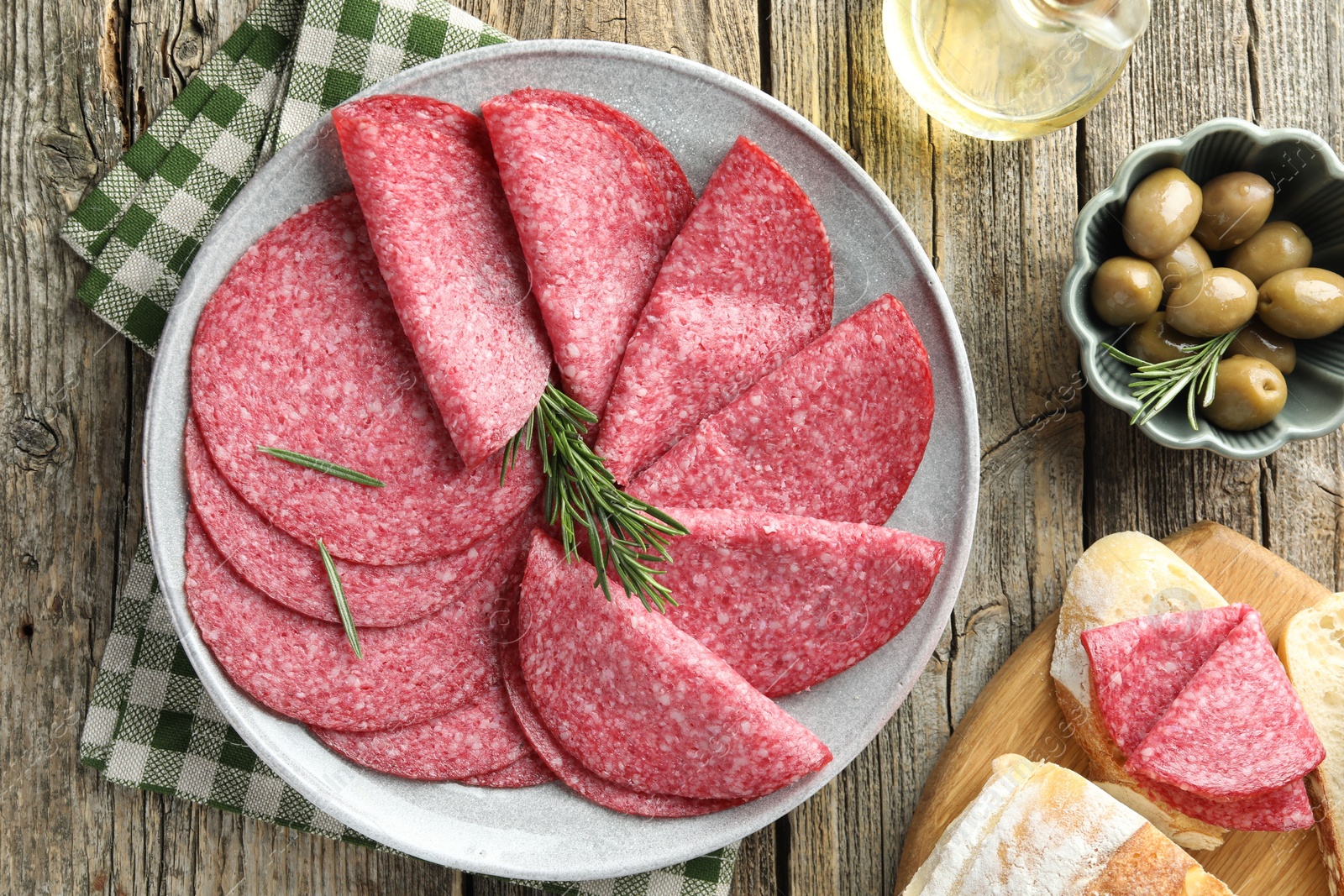 Photo of Slices of delicious sausage with rosemary served on wooden table, flat lay
