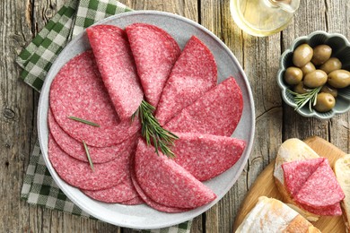 Photo of Slices of delicious sausage with rosemary served on wooden table, flat lay