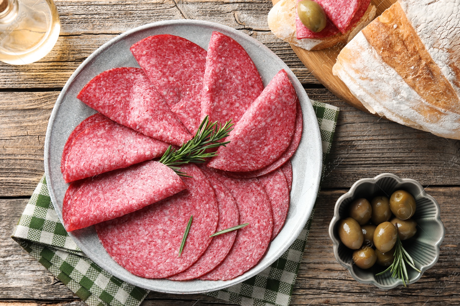 Photo of Slices of delicious sausage with rosemary served on wooden table, flat lay