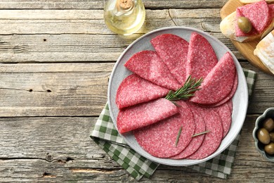 Photo of Slices of delicious sausage with rosemary served on wooden table, flat lay. Space for text