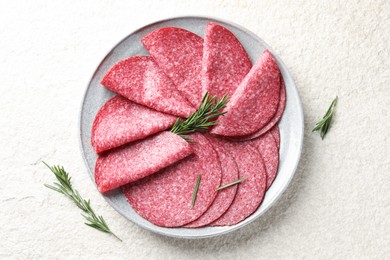 Photo of Slices of delicious sausage with rosemary served on white textured table, top view