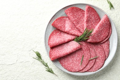 Photo of Slices of delicious sausage with rosemary served on white textured table, top view. Space for text