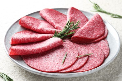 Photo of Slices of delicious sausage with rosemary served on white textured table, closeup