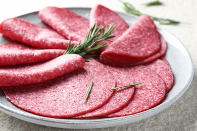 Photo of Slices of delicious sausage with rosemary served on white textured table, closeup