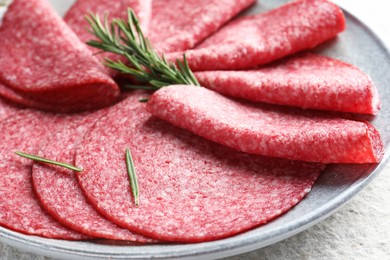 Photo of Slices of delicious sausage with rosemary served on white textured table, closeup