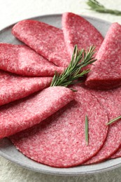 Photo of Slices of delicious sausage with rosemary served on white textured table, closeup