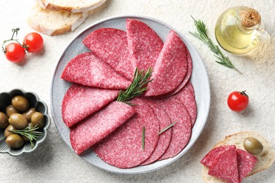 Photo of Slices of delicious sausage with rosemary served on white textured table, flat lay